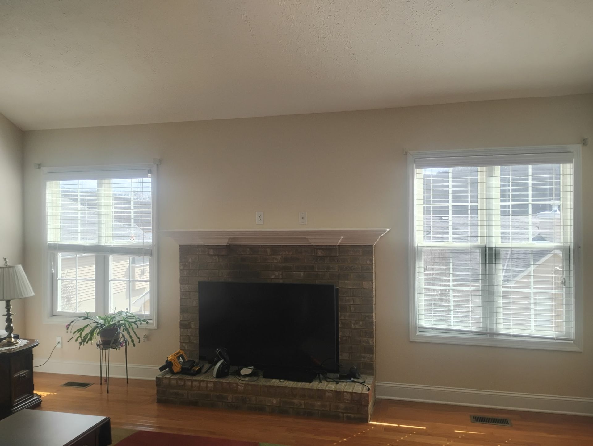 A fireplace with a stone surround and television sits centered between two windows in a room with light-colored walls.