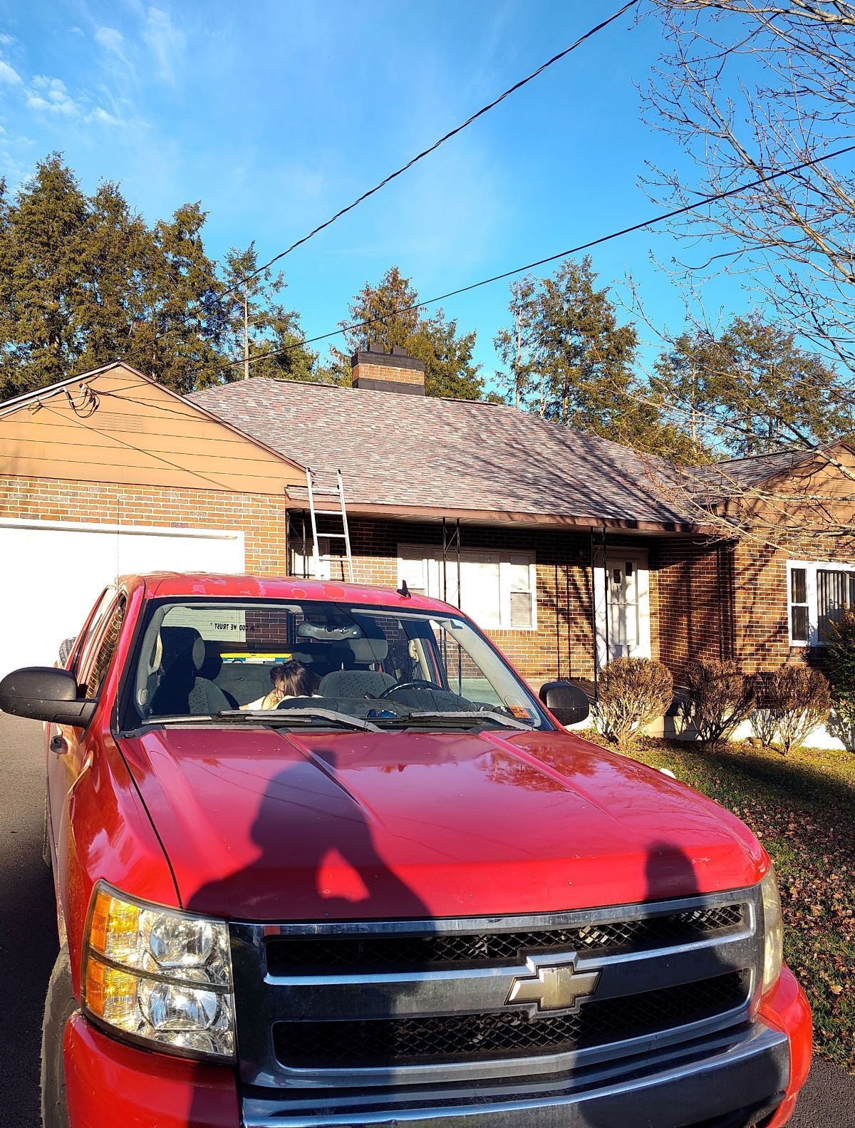A bright red Chevrolet pickup truck parked in front of a house undergoing roof repairs on a sunny day.