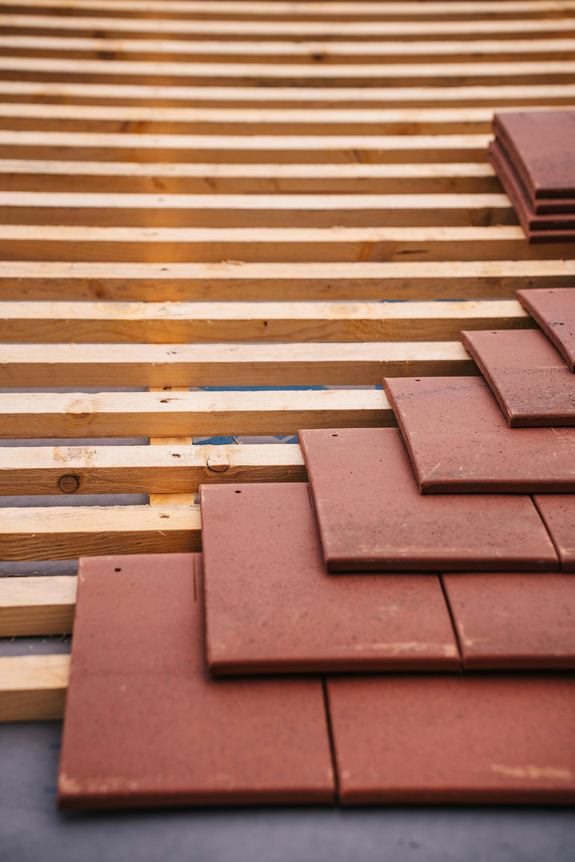 Red clay tiles are being installed on a wooden roof framework.