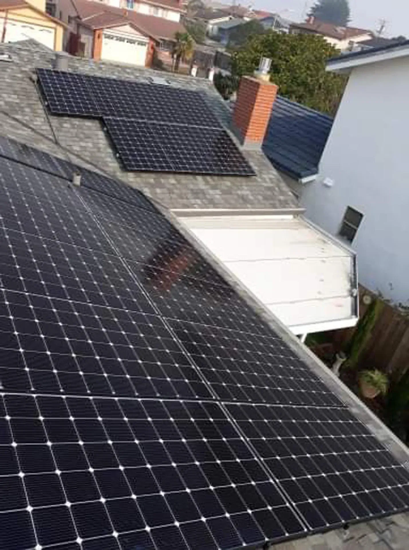 A high-angle view of solar panels covering two sections of a residential shingled roof with a brick chimney.