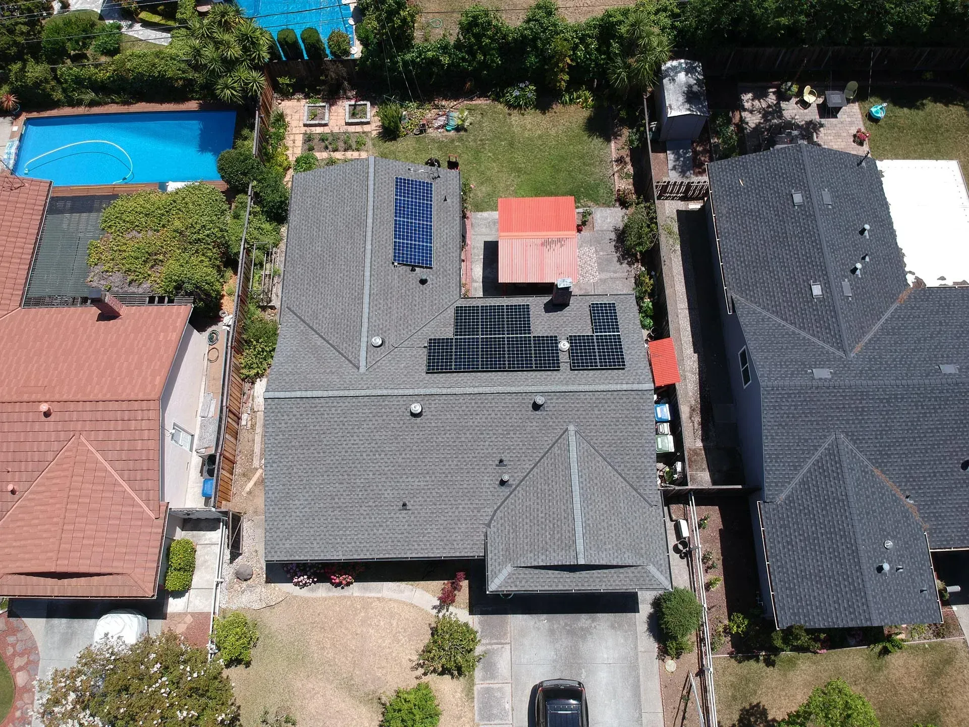 Aerial view of a residential house with a dark shingled roof, solar panels, and a backyard pool.