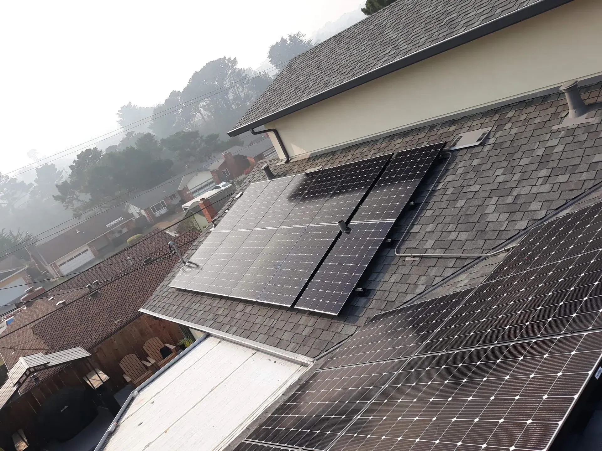 Solar panels mounted on a dark shingled residential roof on a foggy day.