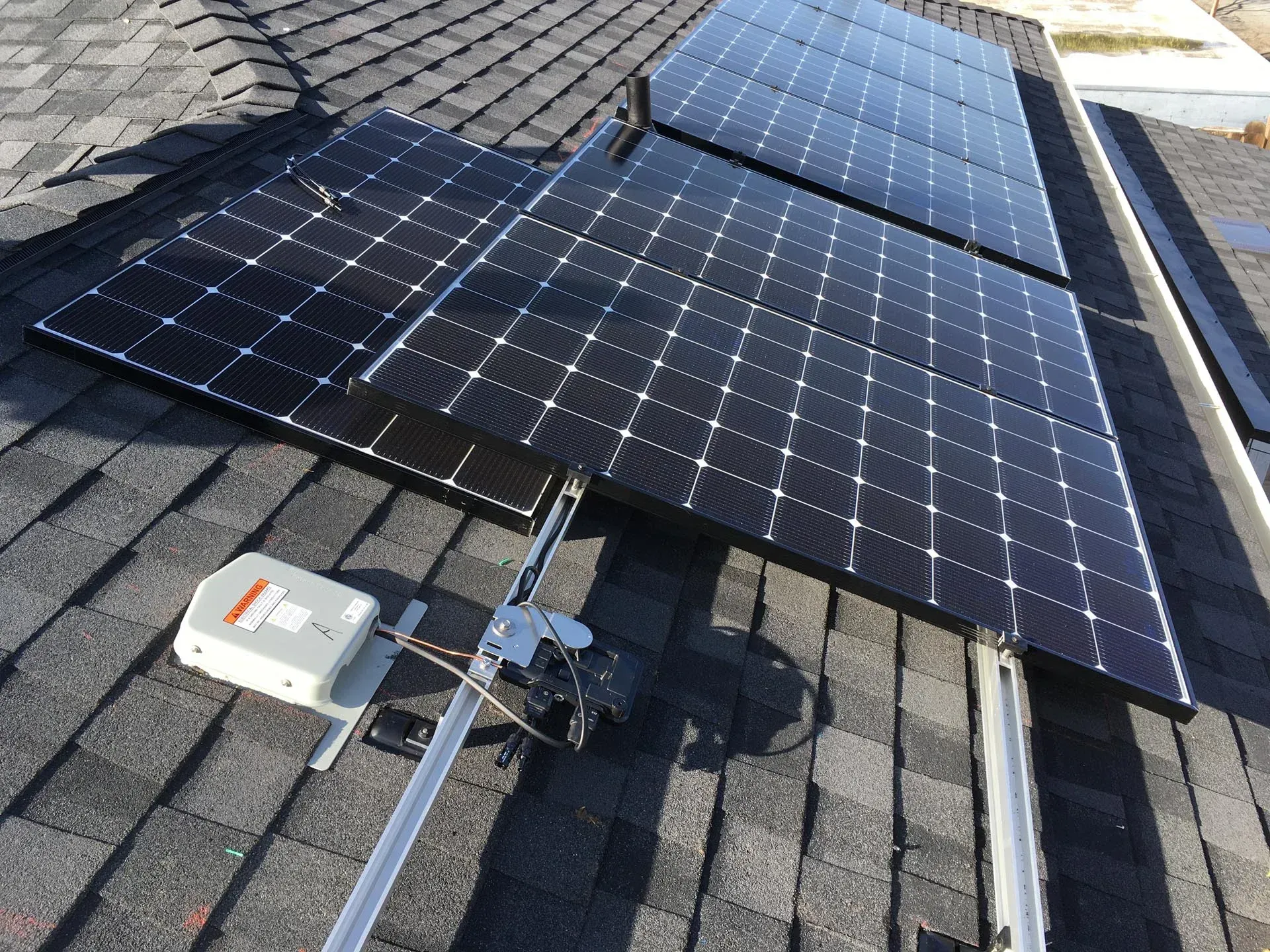 Solar panels mounted on a shingled roof with an attached junction box and electrical wiring.