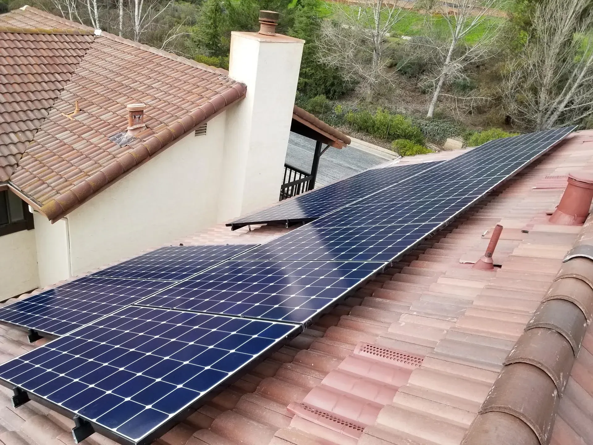 Solar panels installed on a residential roof with terracotta tiles near a house chimney.