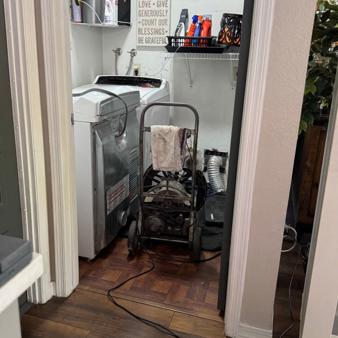 A plumber’s drain auger stands in a laundry room in front of a white washing machine.