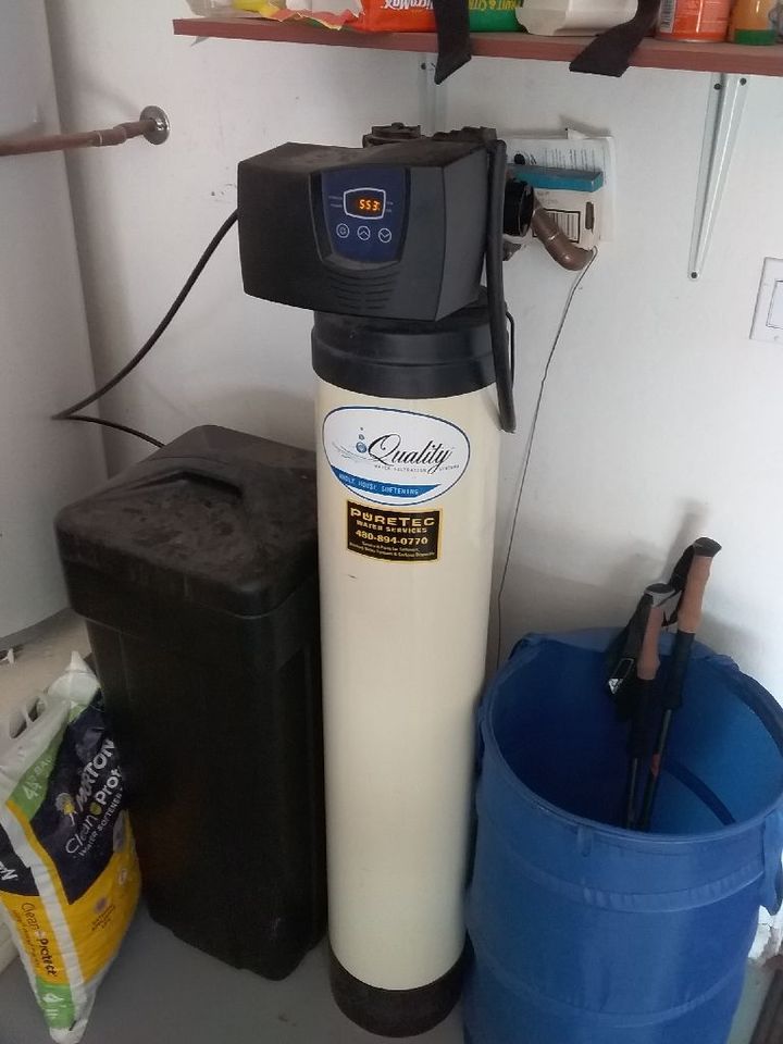 A Kinetico water softener system with a tall, cream-colored tank and a black control head in a residential storage area.