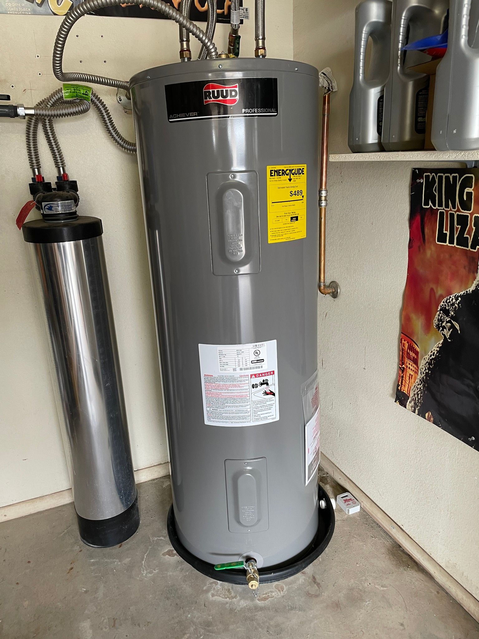A gray water heater stands next to a tall, cylindrical water filter in a garage or utility area.