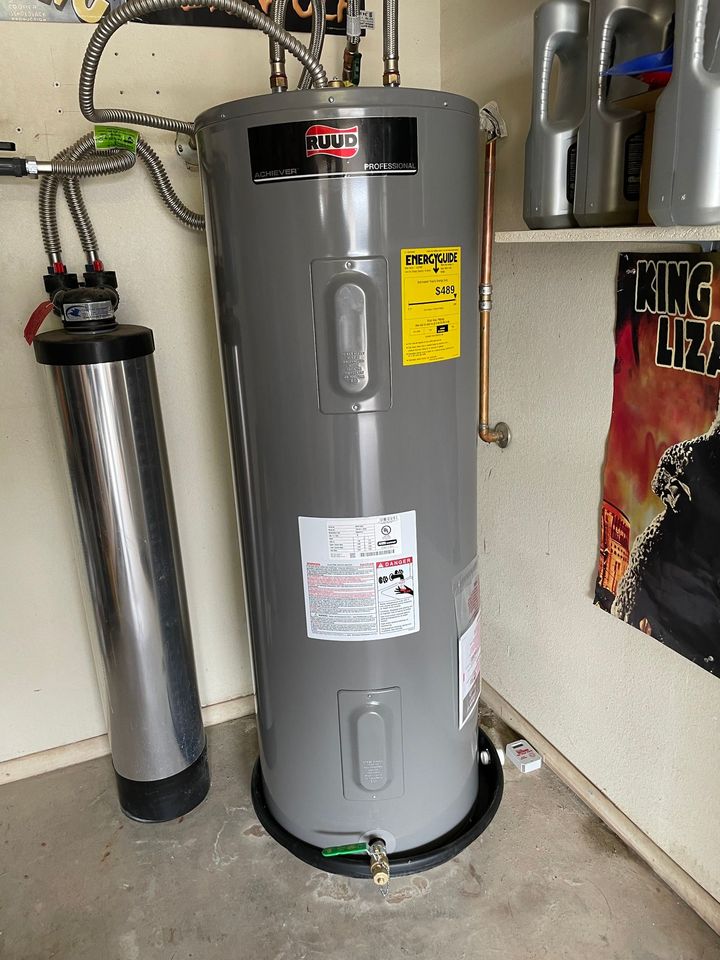 A gray water heater stands next to a tall, cylindrical water filter in a garage or utility area.