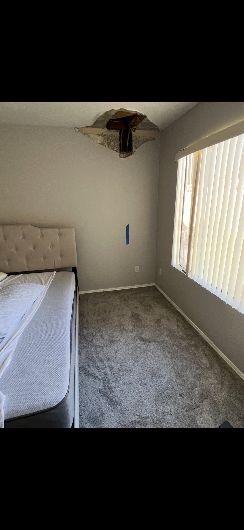 A bedroom with a ceiling collapsed around a light fixture above a bed, showing exposed structural damage.
