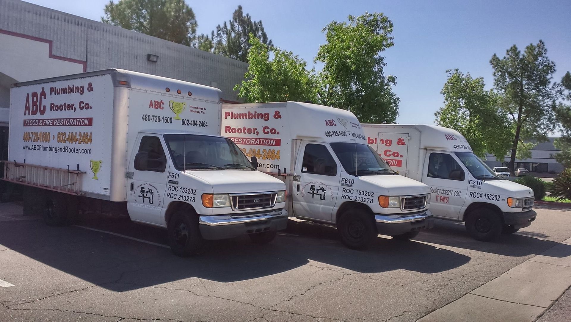 Three white JBC Plumbing & HVAC Co. box trucks parked in a row on an asphalt lot on a sunny day.