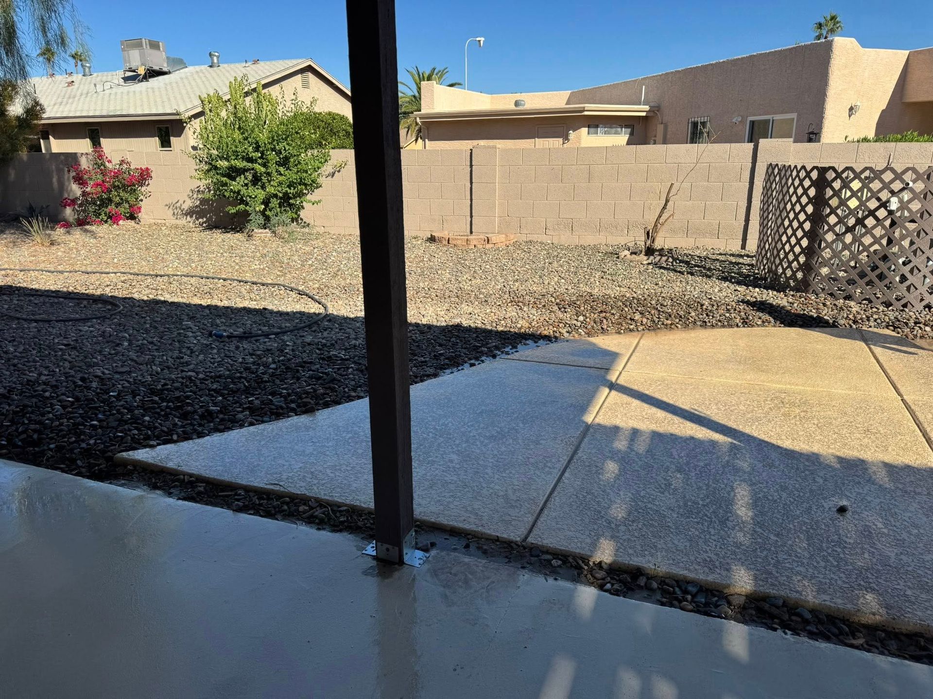 A view from a shaded patio overlooking a backyard with desert landscaping, gravel, and a concrete pathway.