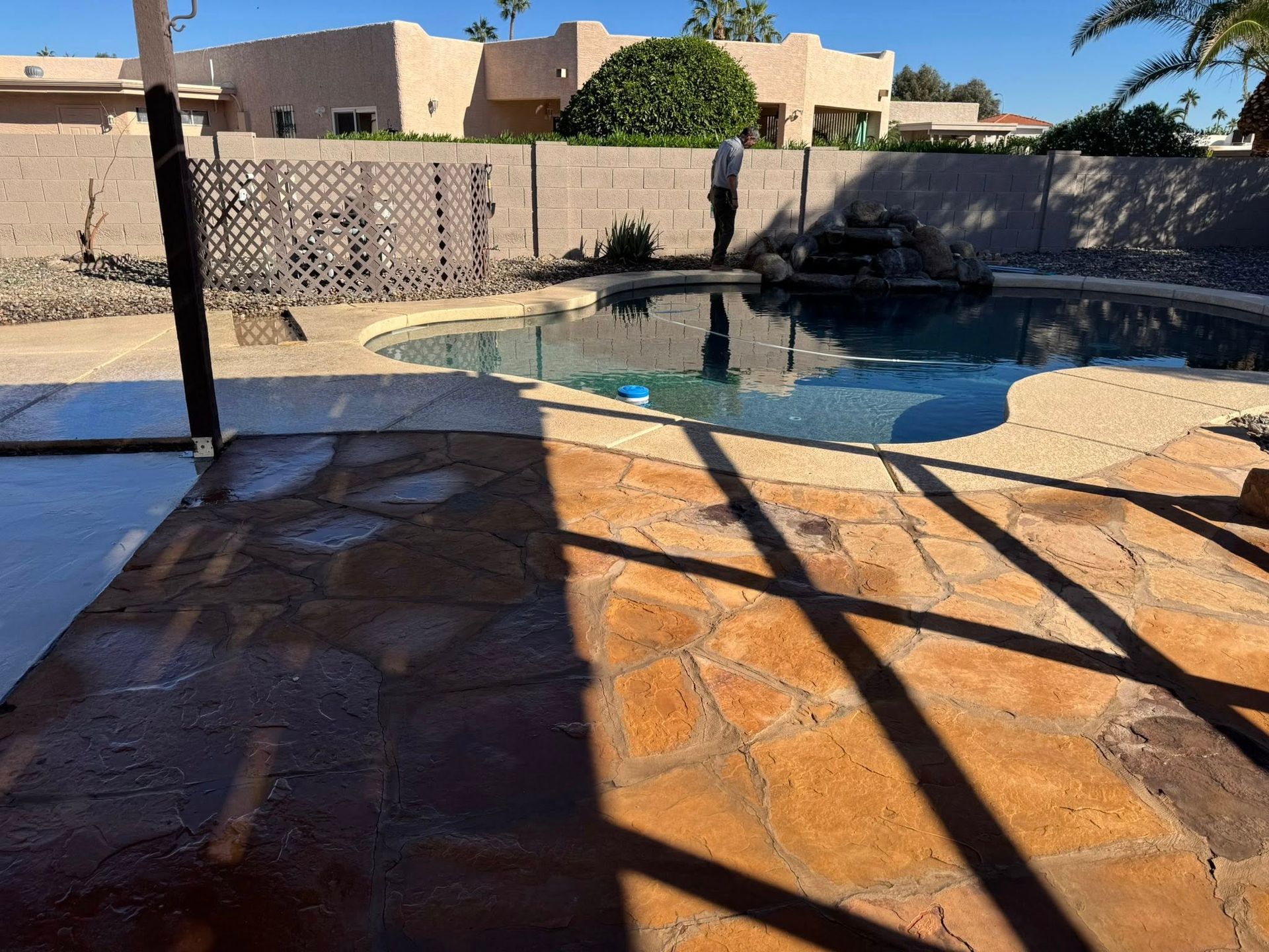 A backyard scene features a swimming pool with a rock water feature, a flagstone patio, and a person standing nearby.