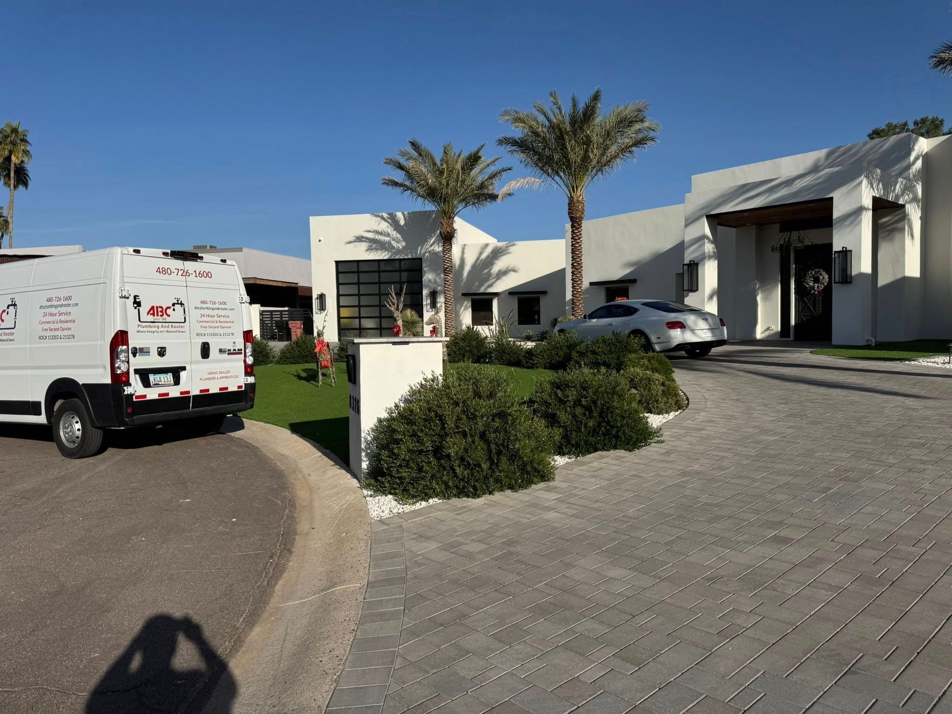 A white service van parked in front of a modern white house with palm trees and a paved driveway under a blue sky.