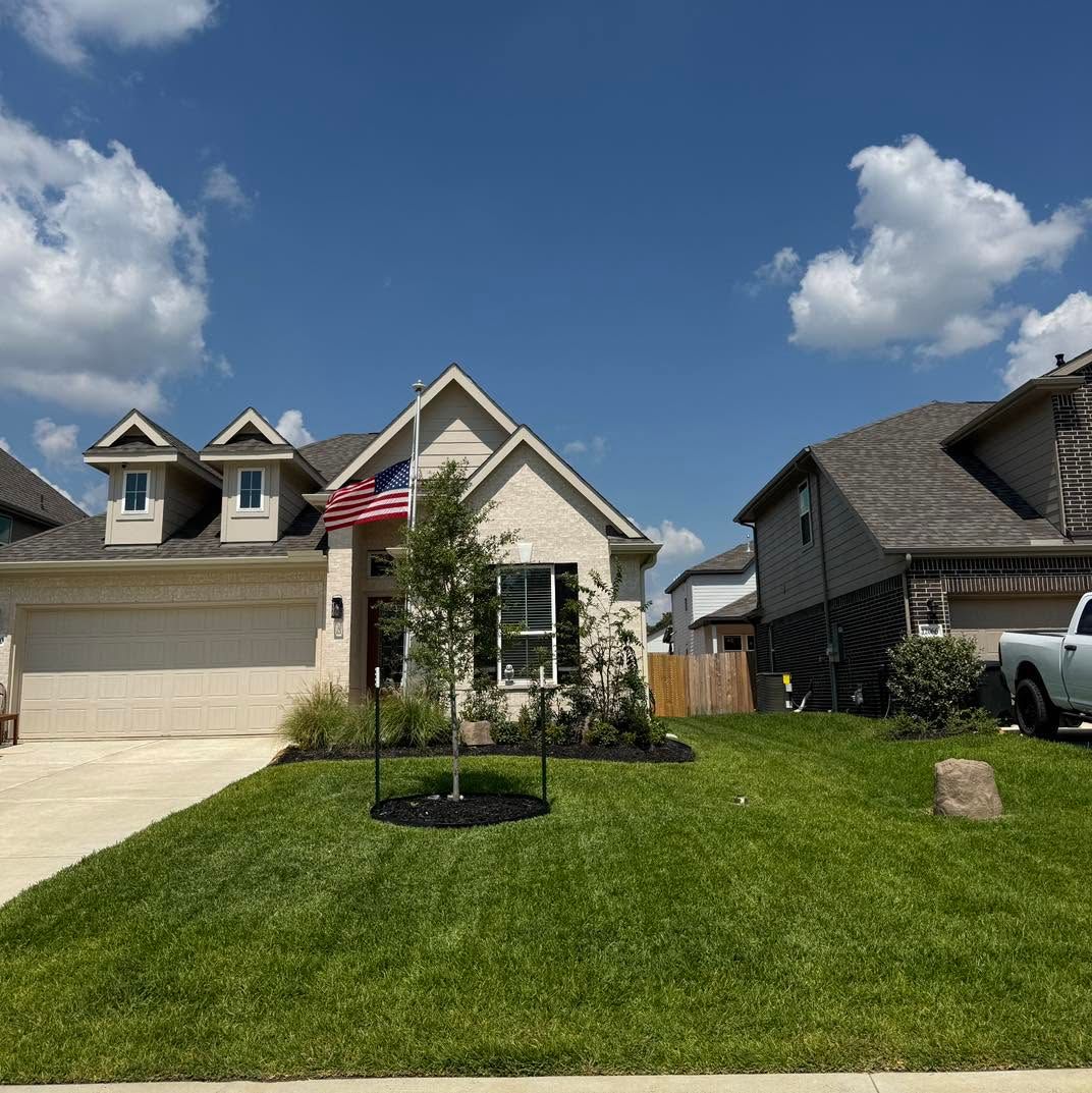Suburban house with American flag, green lawn, and partly cloudy blue sky