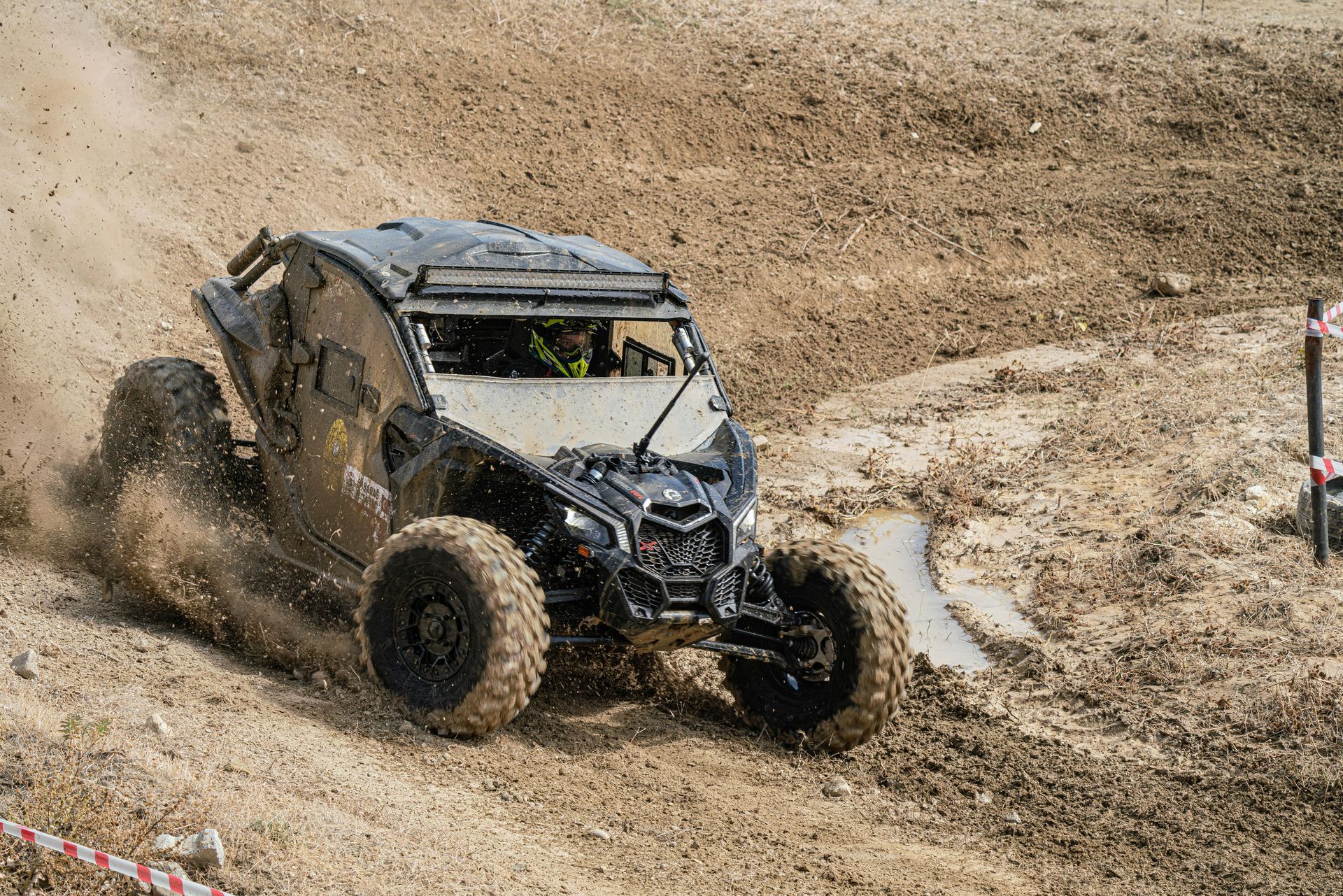Off-road vehicle racing through muddy terrain, kicking up dirt.