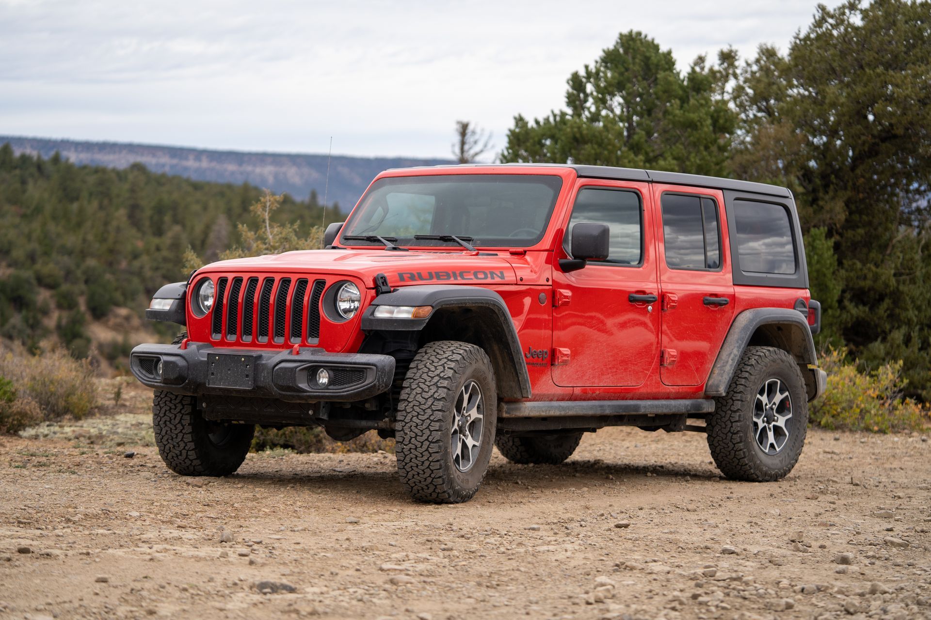 Red Jeep Wrangler parked on a dirt trail with mountains and trees in the background