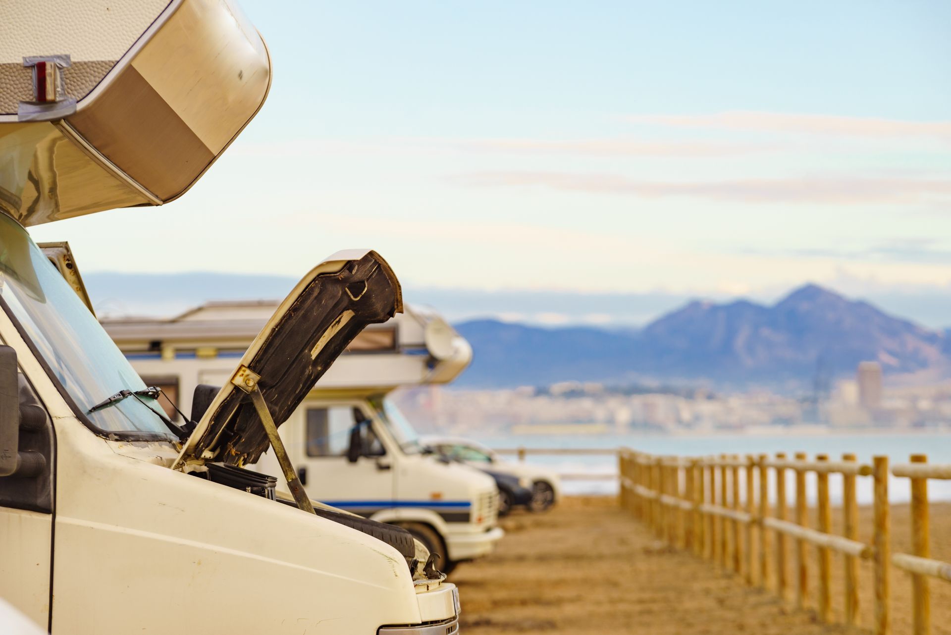 RV campers parked by a lakeside road with open hatches and mountains in the distance