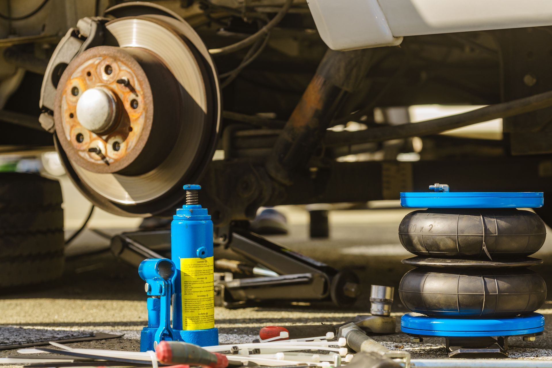 Car brake repair with wheel, brake rotor, tools, and blue jack stand in a garage