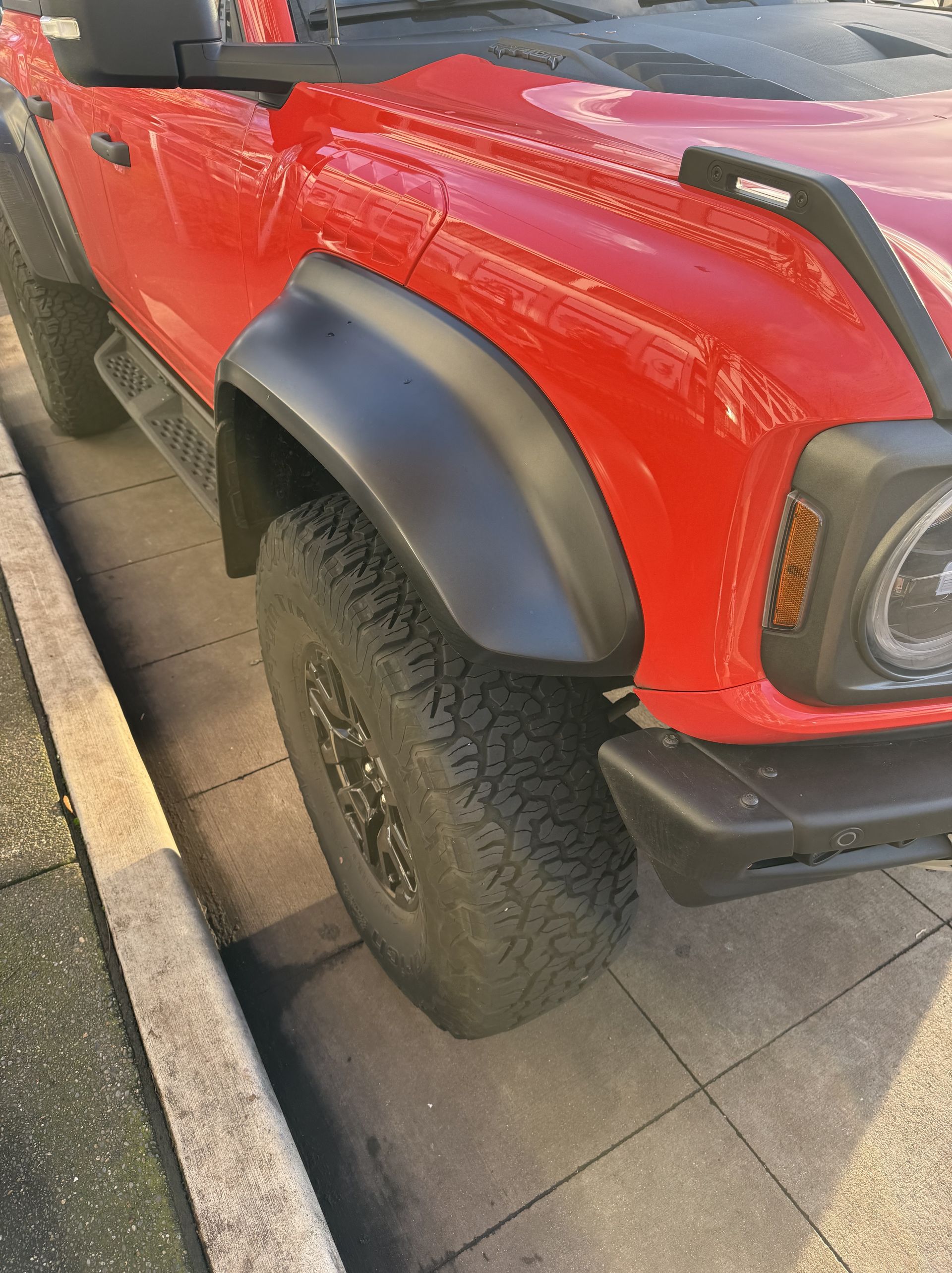 Red off-road SUV with black fender flare parked on tiled pavement, front side view