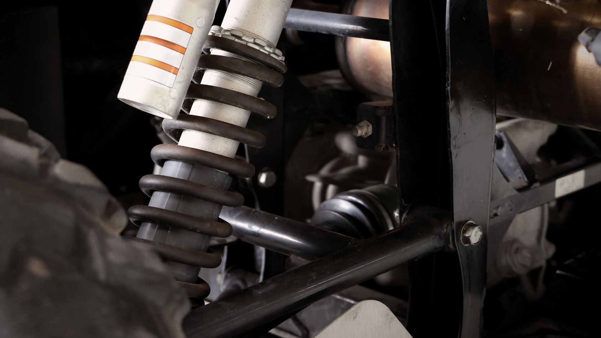 Close-up of a car’s rear suspension spring and shock absorber with dark metal components.