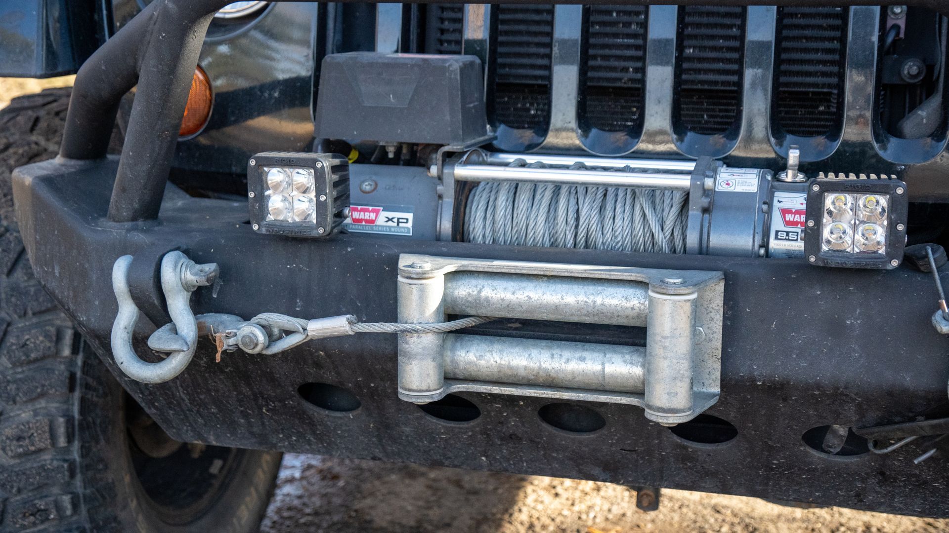 Close-up of a black Jeep front bumper with winch, tow hooks, and off-road lights