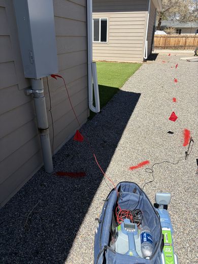 Marked side yard walkway with red flags, gravel, and a tool bag near a house foundation.