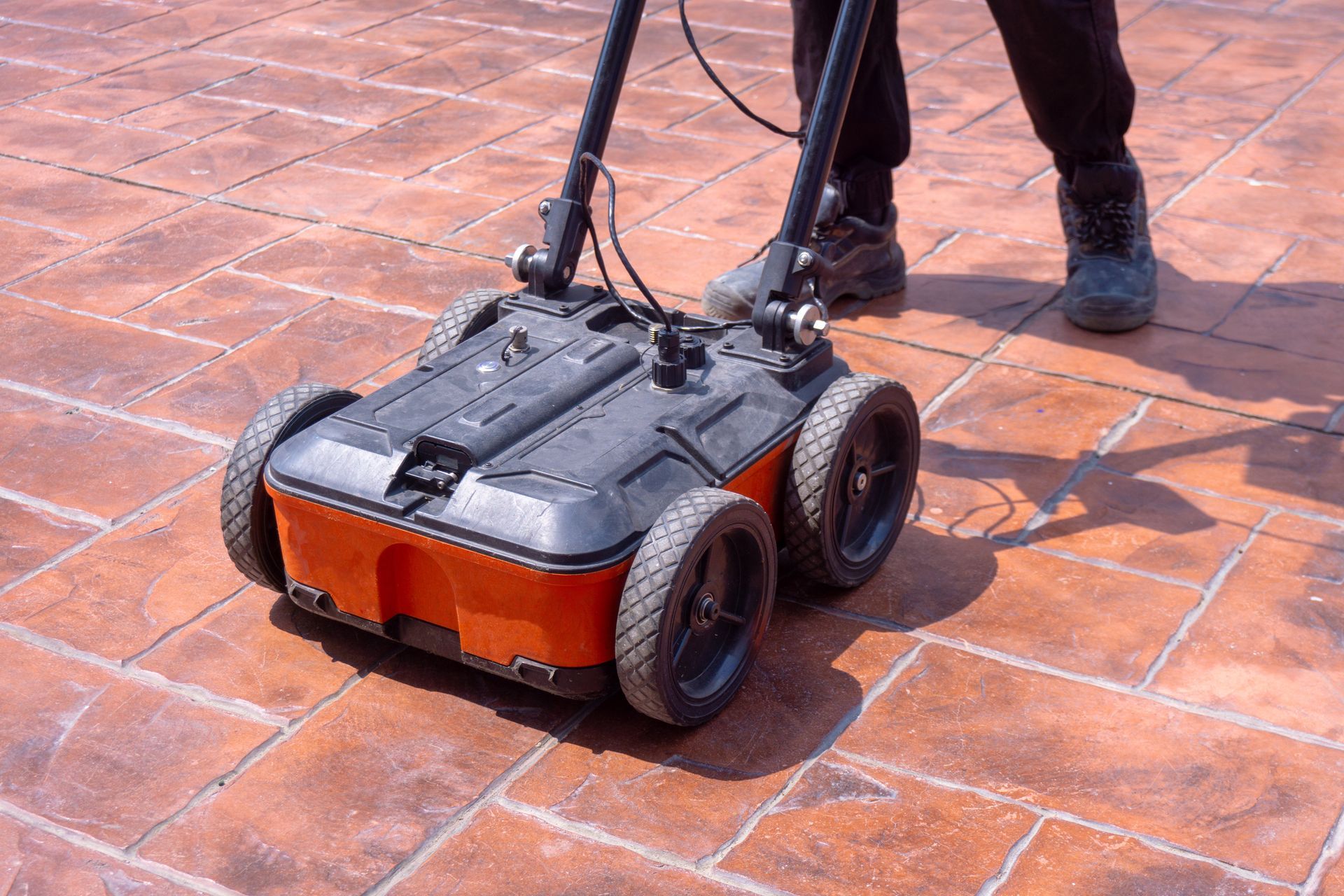 Person using a wheeled floor-cleaning machine on a tiled patio