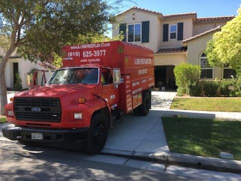 Red junk removal truck parked in driveway of two-story house.