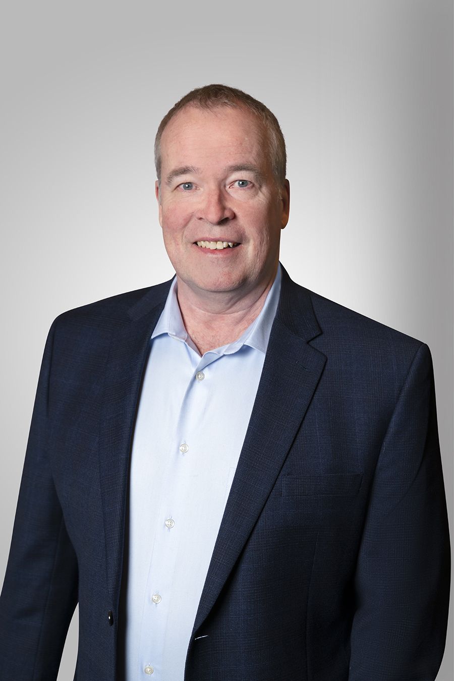 Smiling man in blue blazer and shirt, against a gray gradient background.