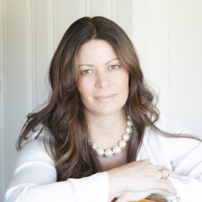 Woman with long brown hair, wearing a white shirt and pearl necklace, smiling.