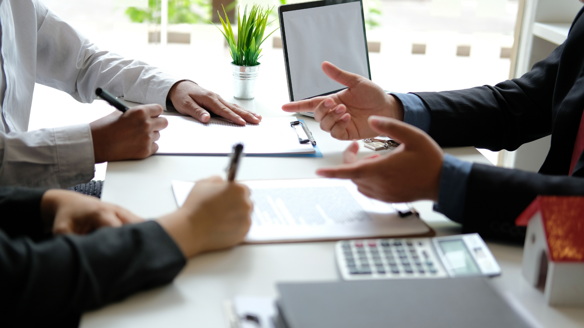 People in a meeting discussing papers at a conference table with a calculator and laptop nearby