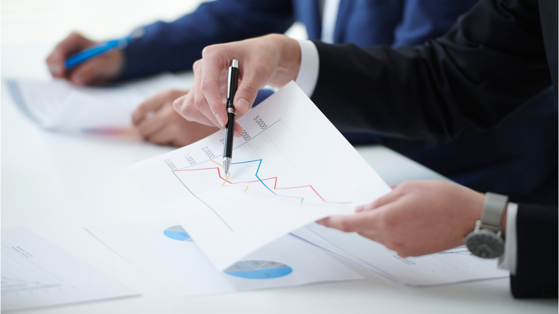 Hands pointing at a chart with blue and red line graphs on papers in a meeting room