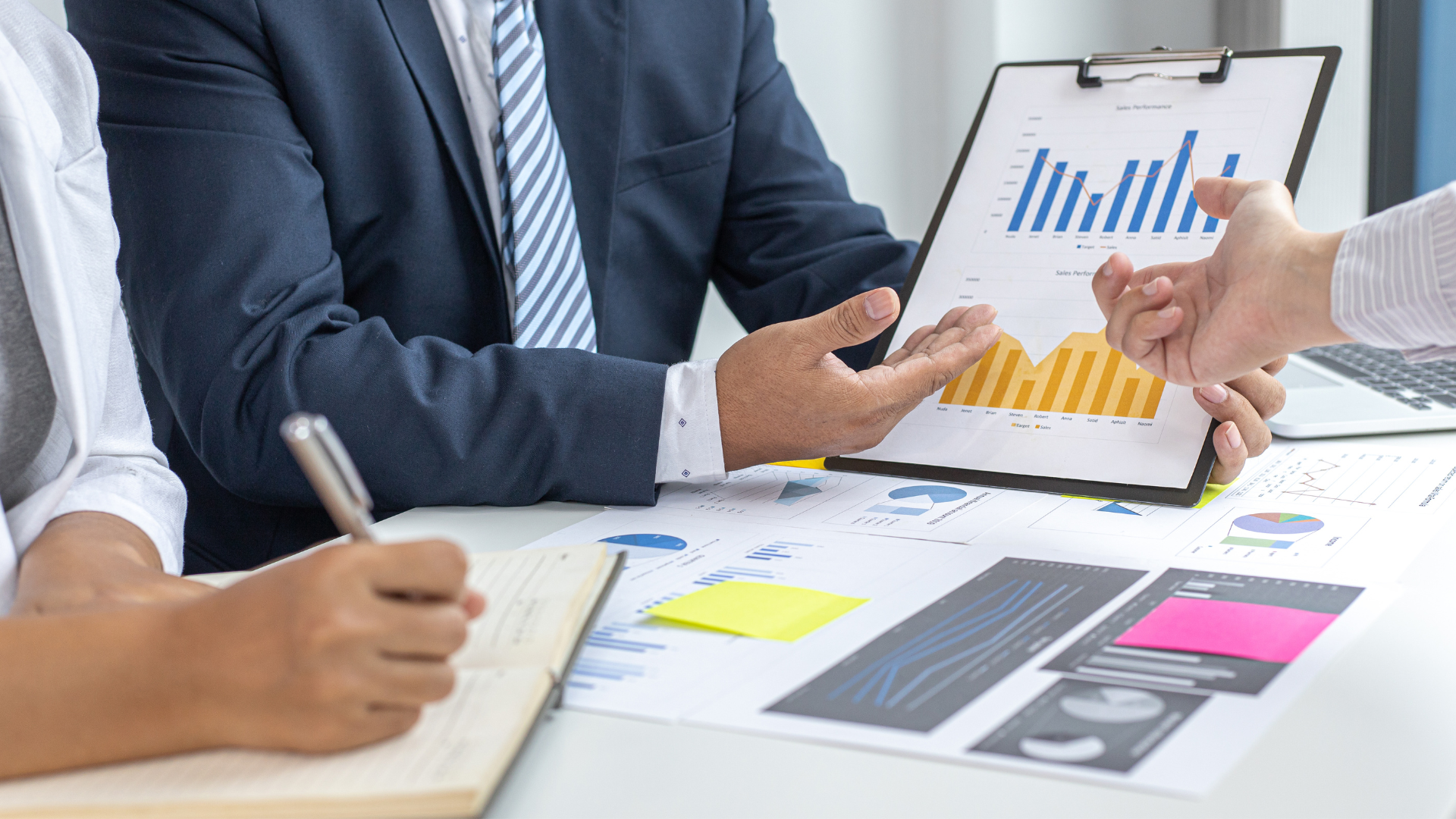 Business meeting with people reviewing charts and documents at a desk.