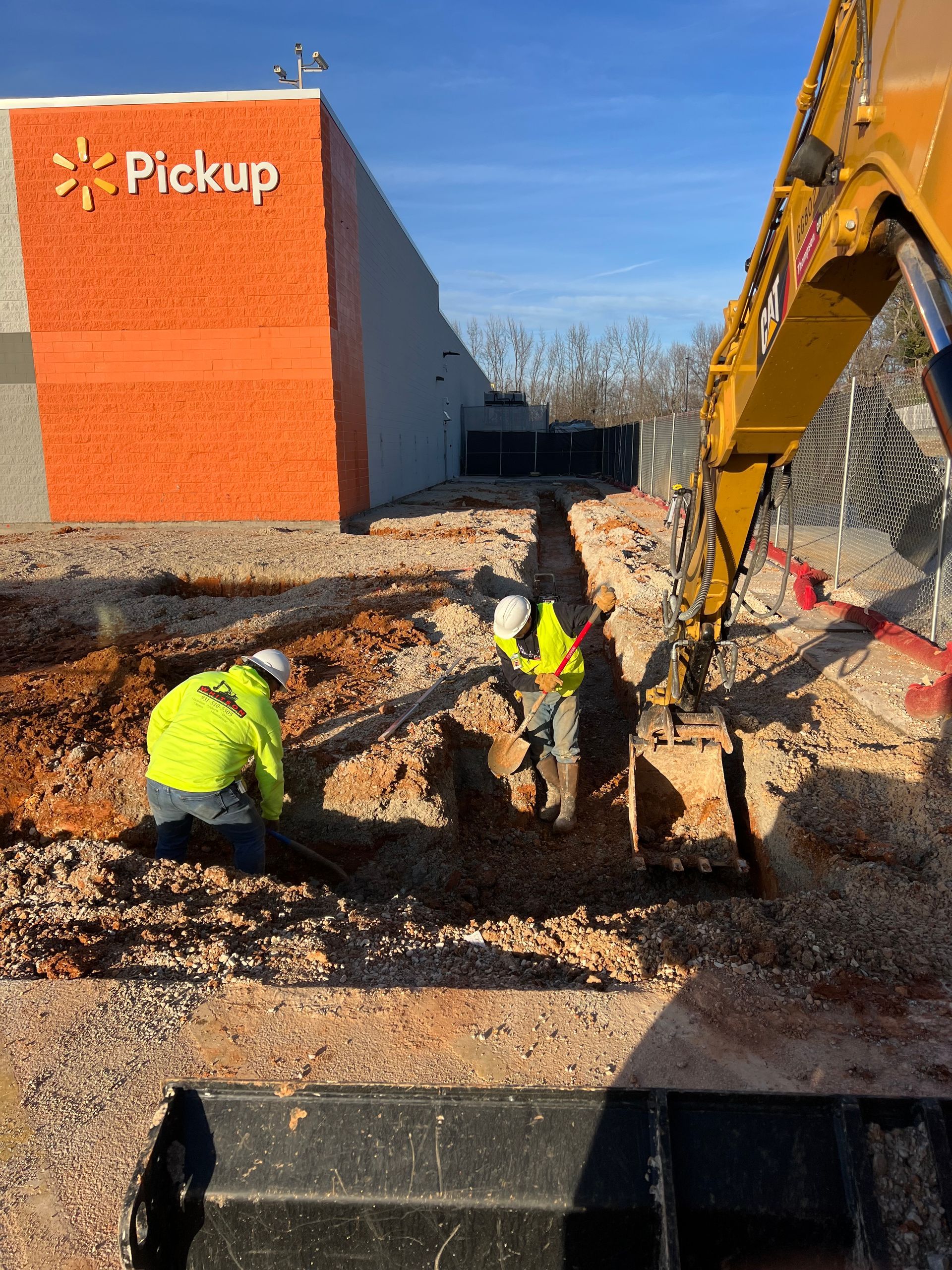 Two construction workers are digging in the dirt in front of a walmart store.