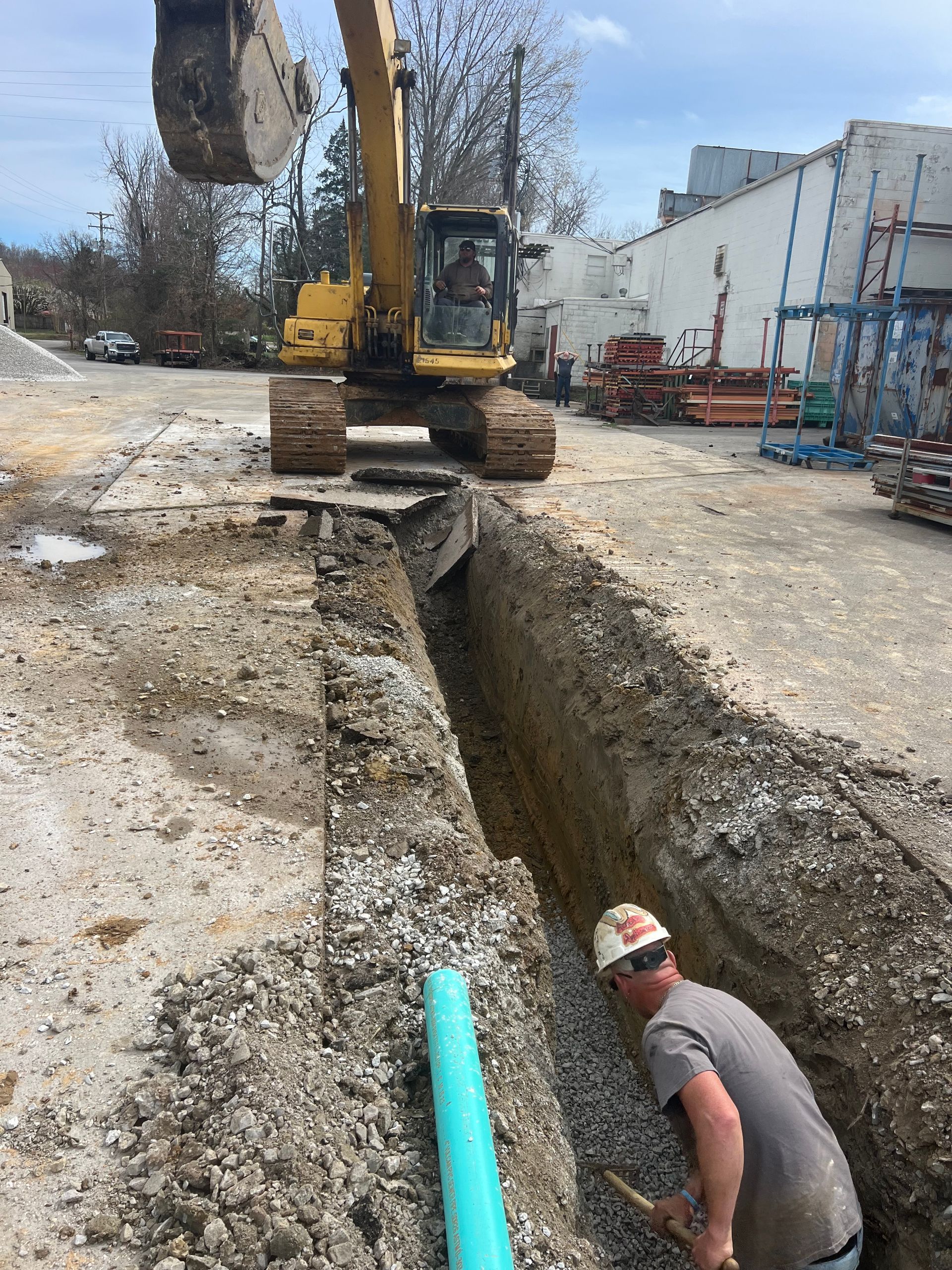 A man is digging a trench next to a yellow excavator.