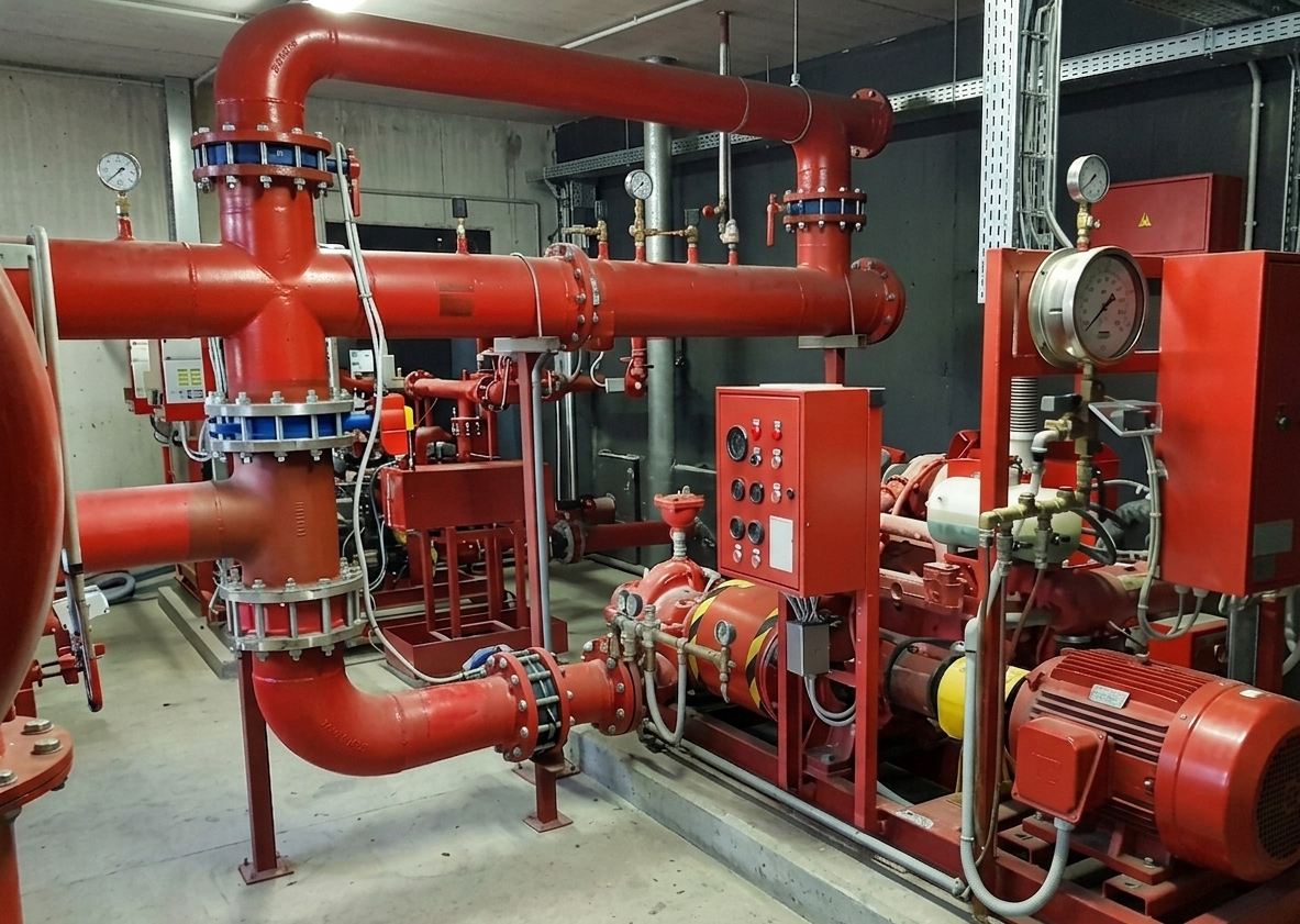 Tubature e pompe antincendio industriali rosse in un locale tecnico.