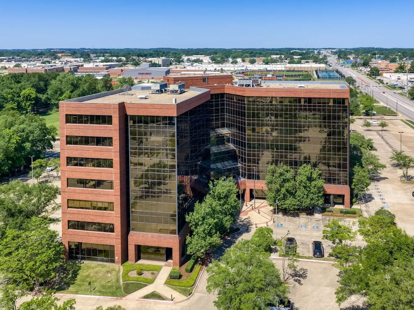 Aerial view of a red-brick office building with reflective glass windows, surrounded by trees and a parking lot.