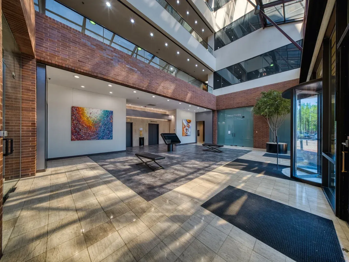 Modern atrium with brick walls, glass railings, skylights, and a colorful wall artwork.
