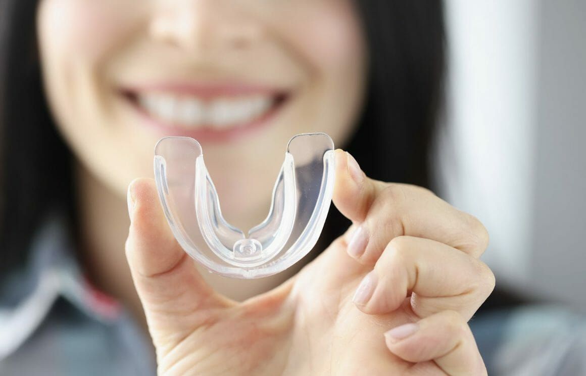 Person holding a clear dental aligner in front of a smiling face