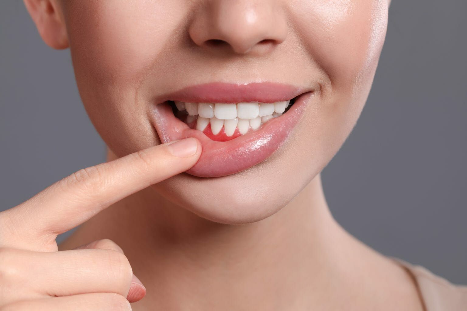 Person pointing to a tooth with red gums, suggesting dental pain or gum irritation