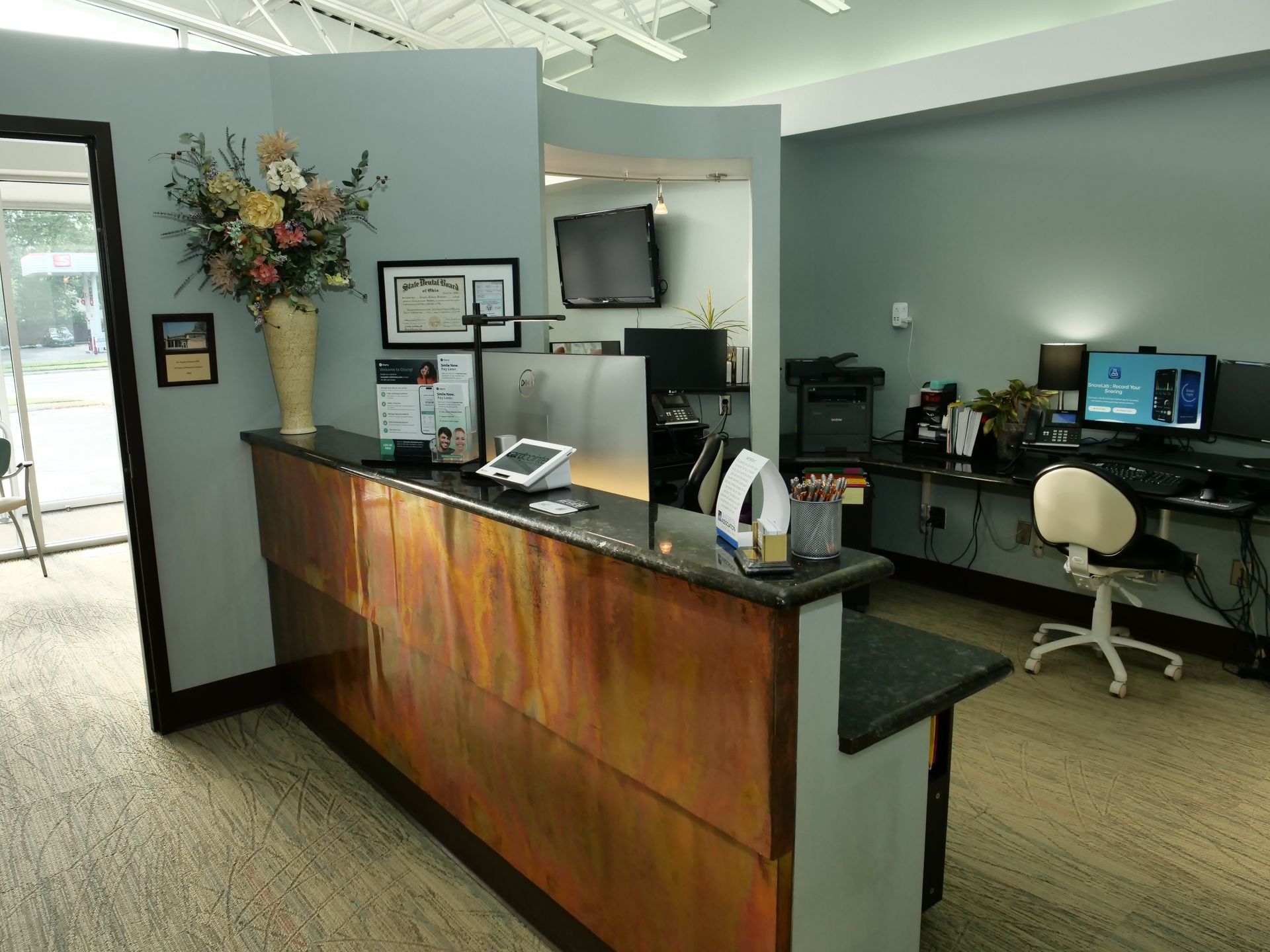 Office reception area with wooden desk, flowers, and workstations in the background