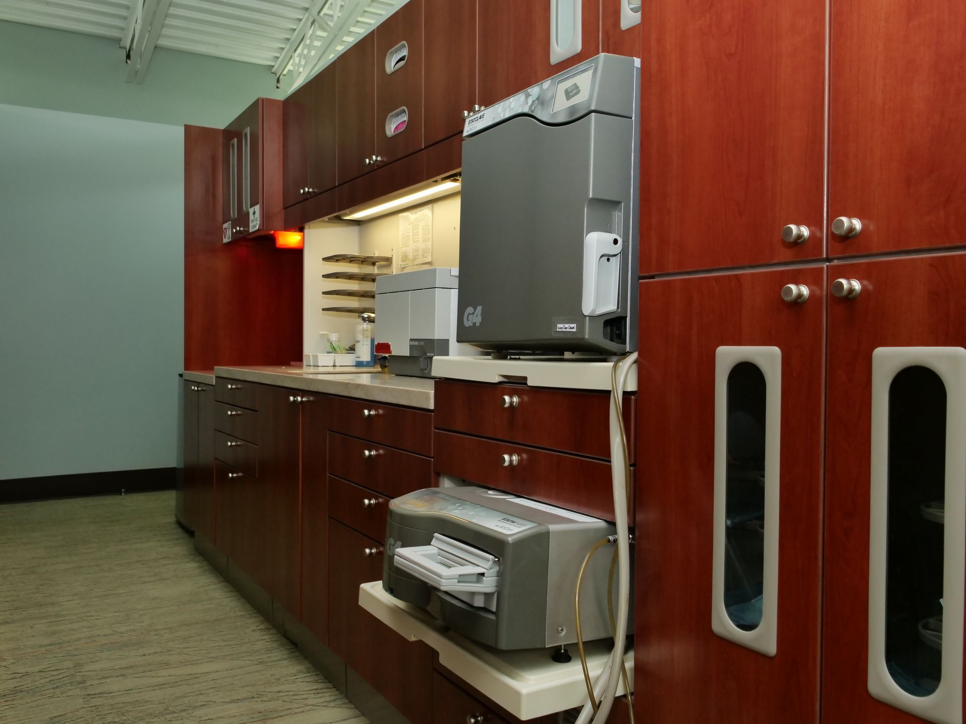 Wood-paneled office kitchenette with cabinets, sink, mini-fridge, microwave, and copier on countertop.