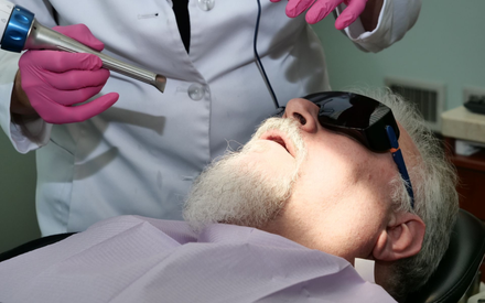 Dental procedure in progress on a patient wearing dark glasses, with gloved clinician holding a tool.