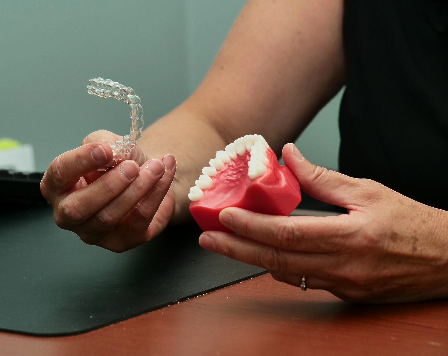 Hands holding clear aligner and red dental model on a table