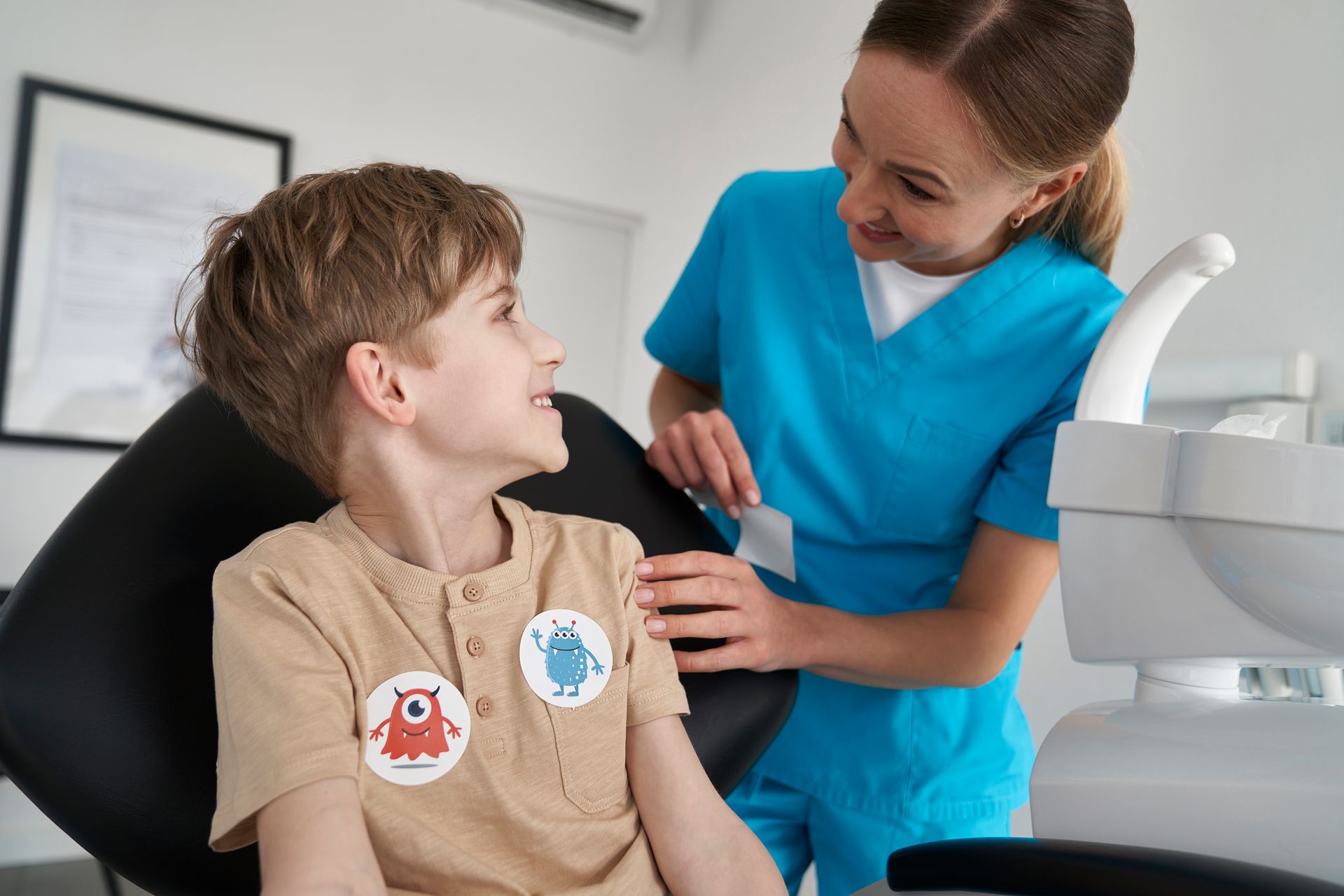 Dental hygienist in blue scrubs smiling at a child in a dental chair during an exam