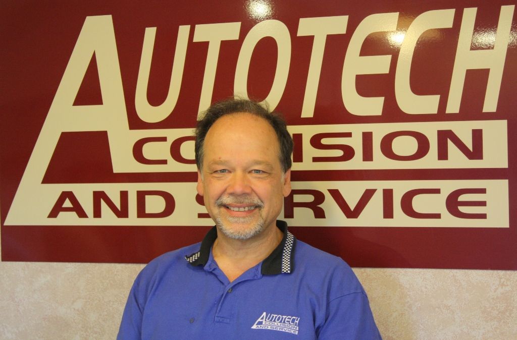 Man standing in front of an Autotech Collision and Service sign, wearing a blue polo and smiling. | Autotech Service