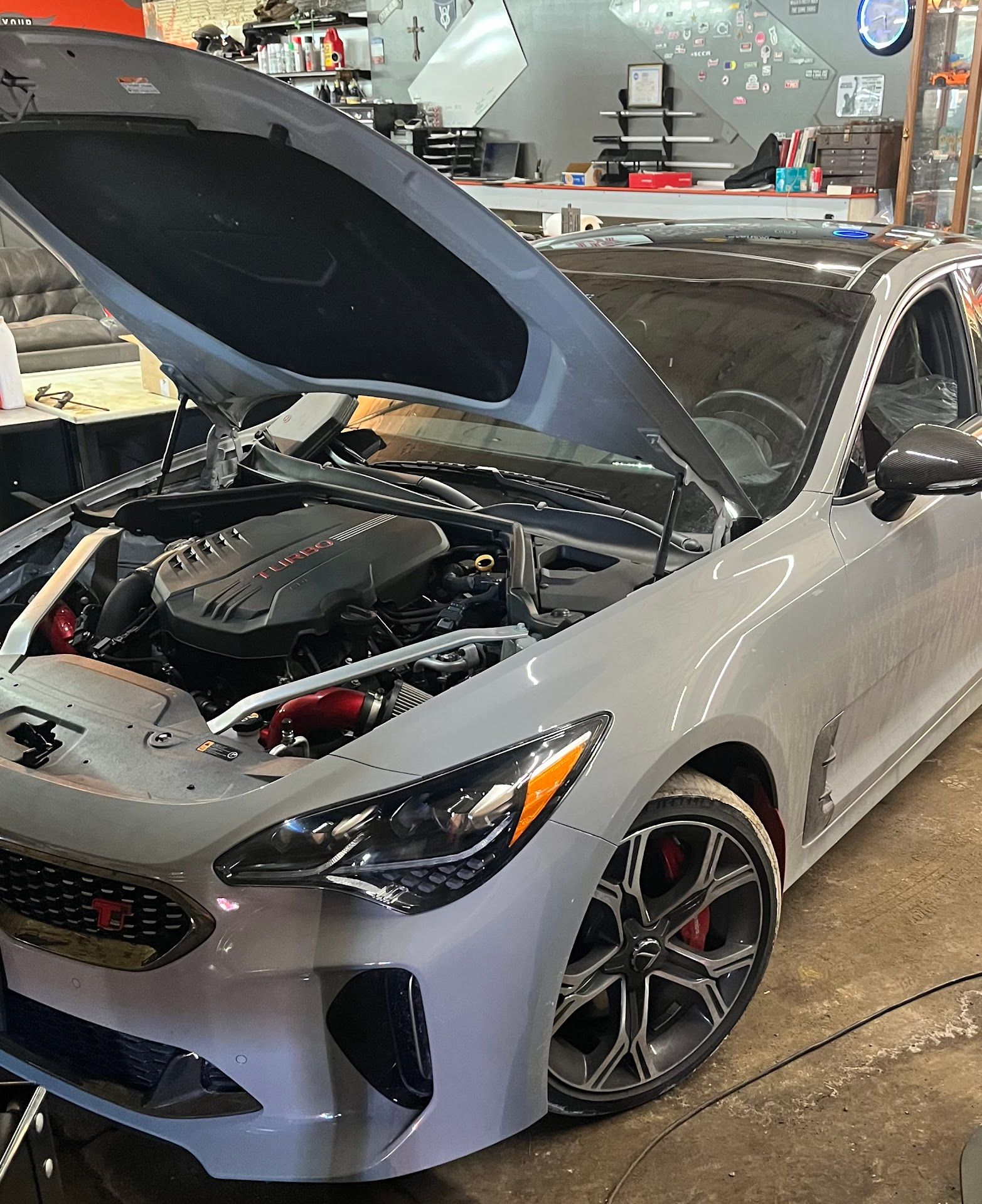 Silver sports car with hood open in an auto shop, showing engine and front wheel. | Autotech Service