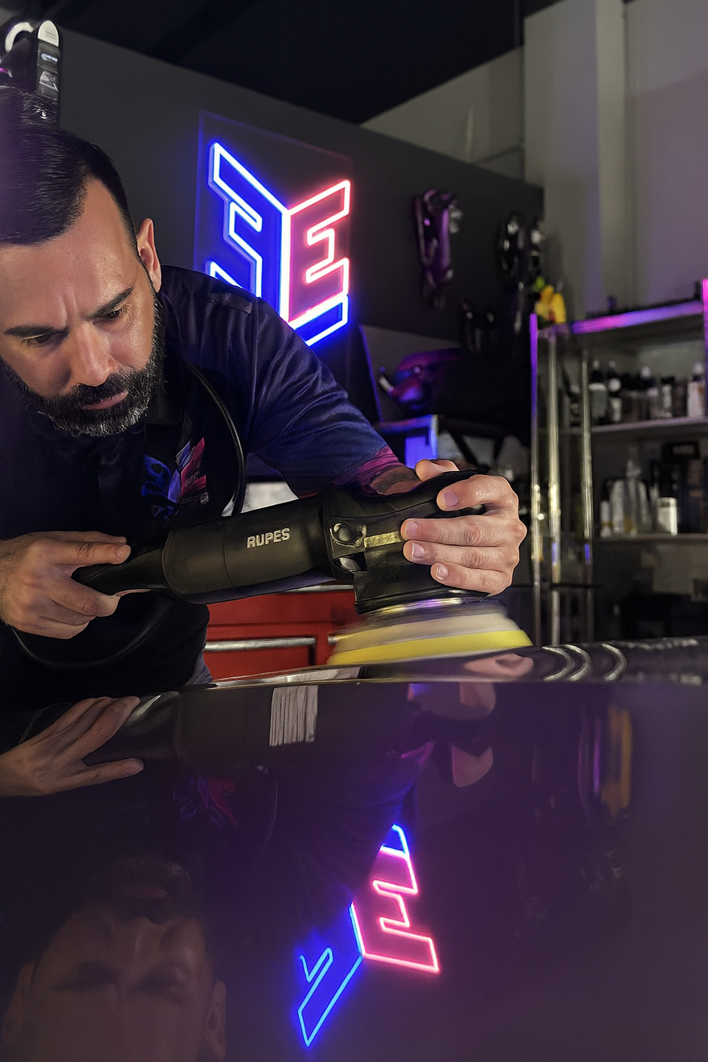 Young man polishes a red car bumper with a machine in a detail shop.