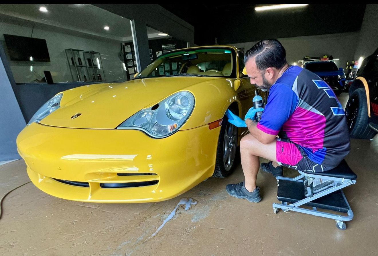 Person cleaning a car seat with a handheld vacuum. The seat is dark gray and the car interior is visible.