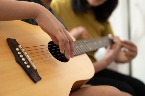Hands playing a natural wood acoustic guitar in a casual indoor setting